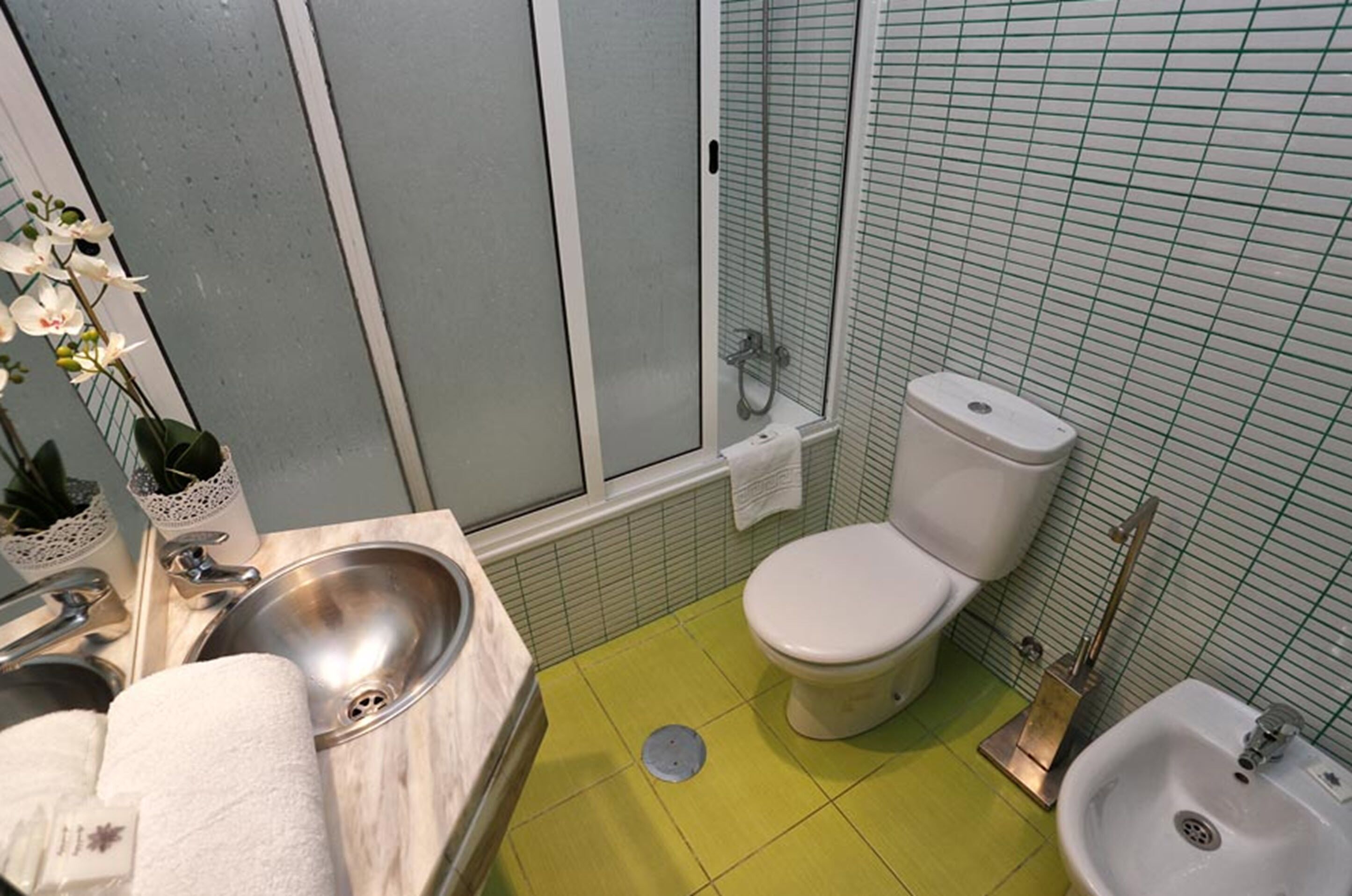 A bathroom with a yellow floor, a sink, a toilet, and a shower.