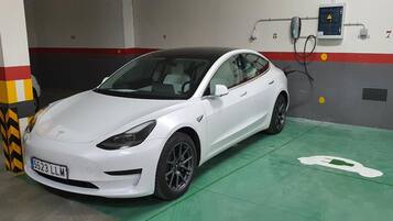 Un Tesla Model 3 blanco en un estacionamiento subterráneo con suelo verde y una estación de carga.