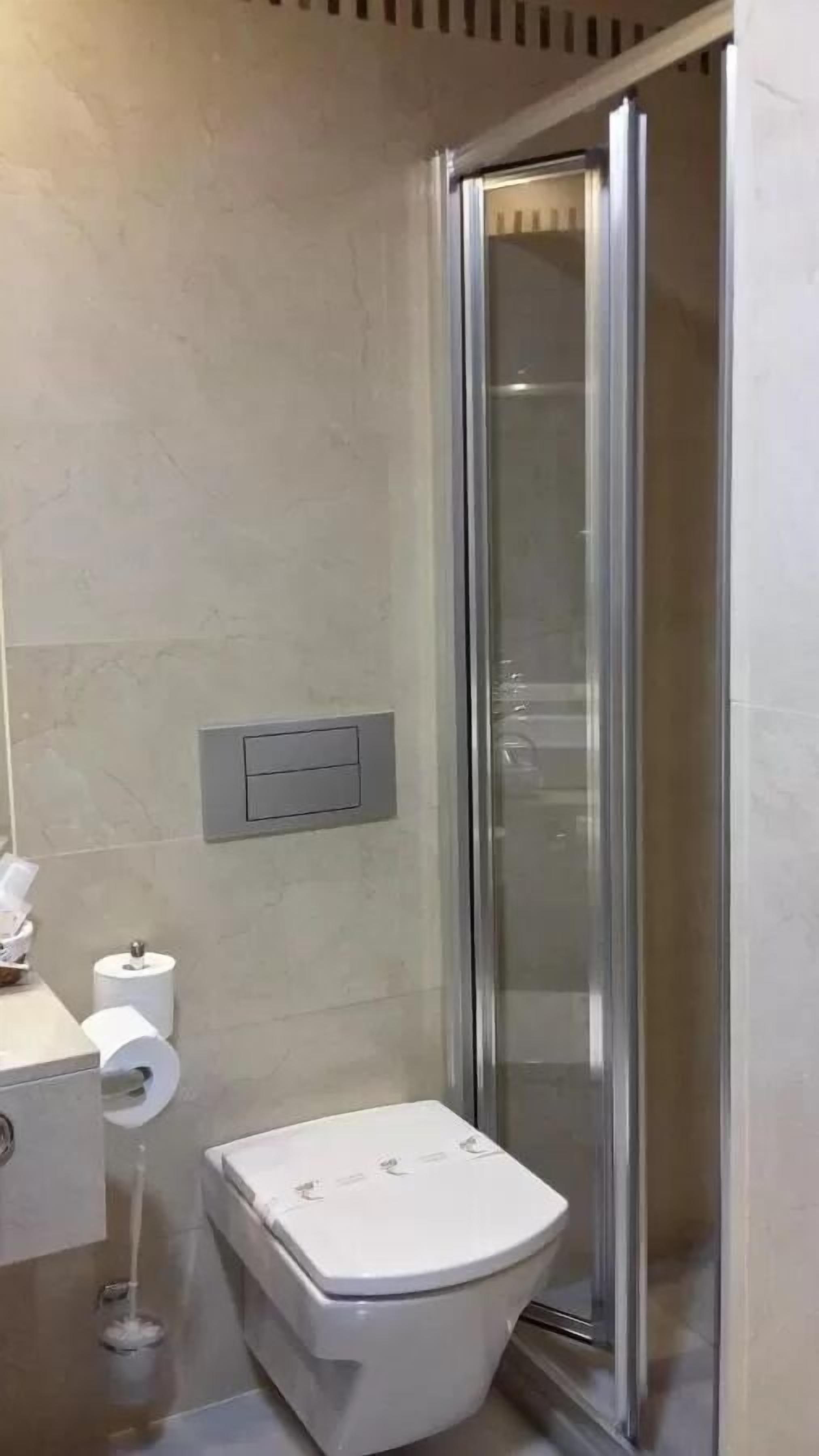 A bathroom with a toilet, a glass shower enclosure, and a wall-mounted toilet paper holder.