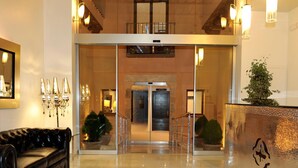 A hotel lobby with a black leather sofa, a reception desk, a glass door entrance, and a polished floor.