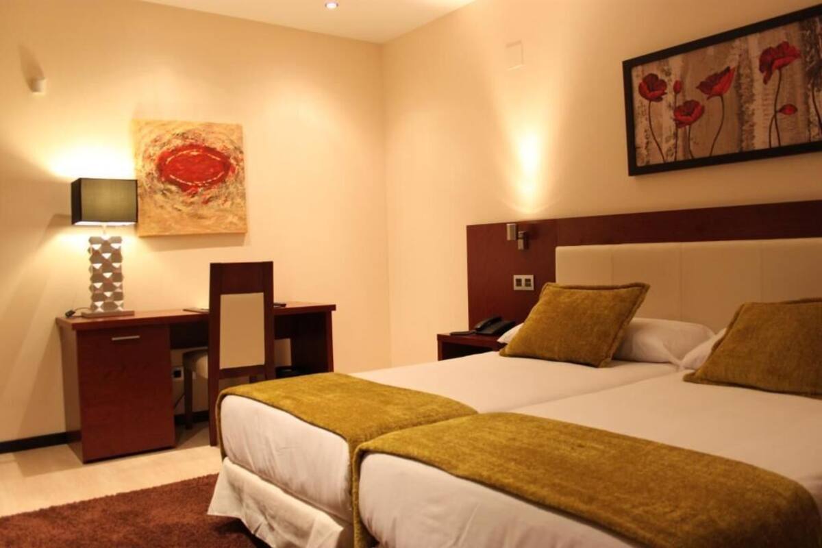 Habitación de hotel con dos camas, un escritorio, una silla, un televisor y obras de arte en las paredes.