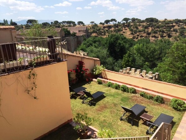Terraza en la azotea con vistas a un paisaje montañoso, que incluye un pequeño jardín con plantas en macetas y una zona de estar con mesas y sillas.