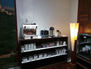 A coffee station with a coffee machine, cups, and a refrigerator.