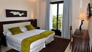 A hotel room with a large bed, two pillows, a nightstand, a desk with a lamp, and a window with curtains.