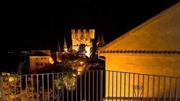 A night view of a building with a lit tower, a fenced area, and a yellow structure with a decorative roof.