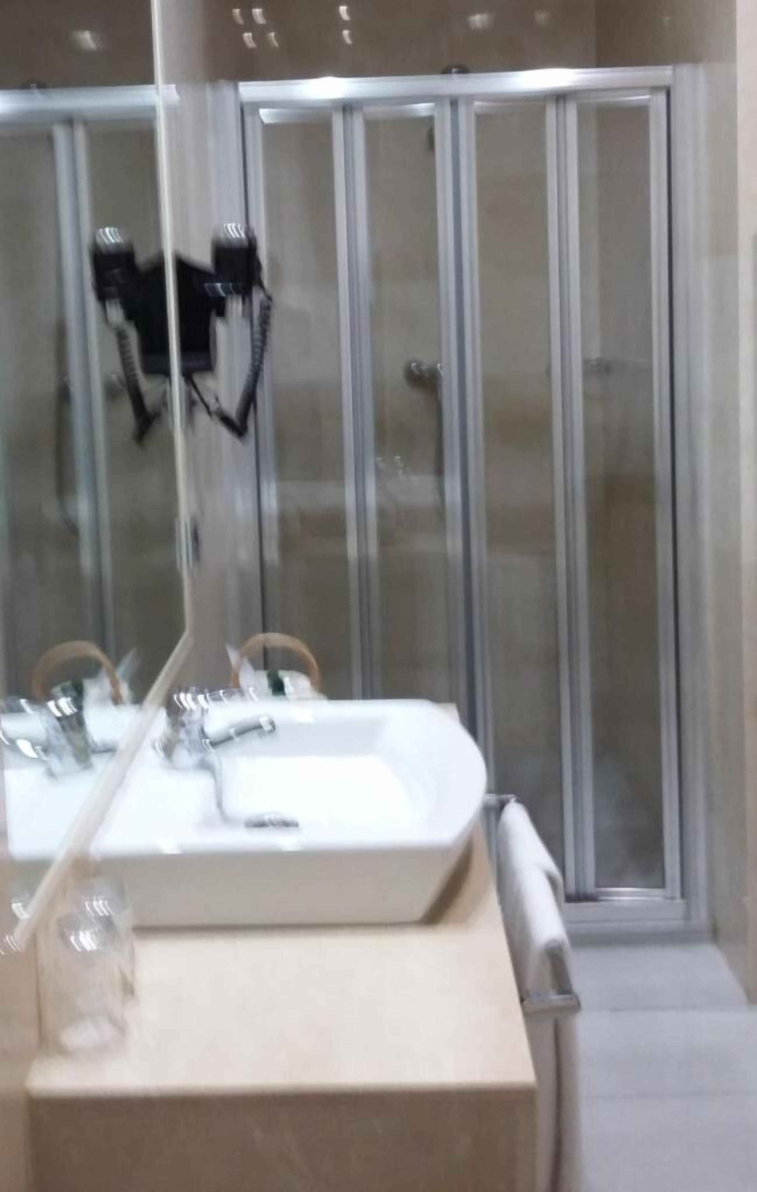 A bathroom with a large mirror, a sink, and a glass shower enclosure.