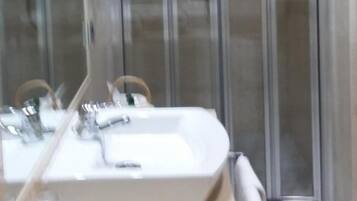 A bathroom with a large mirror, a sink, and a glass shower enclosure.