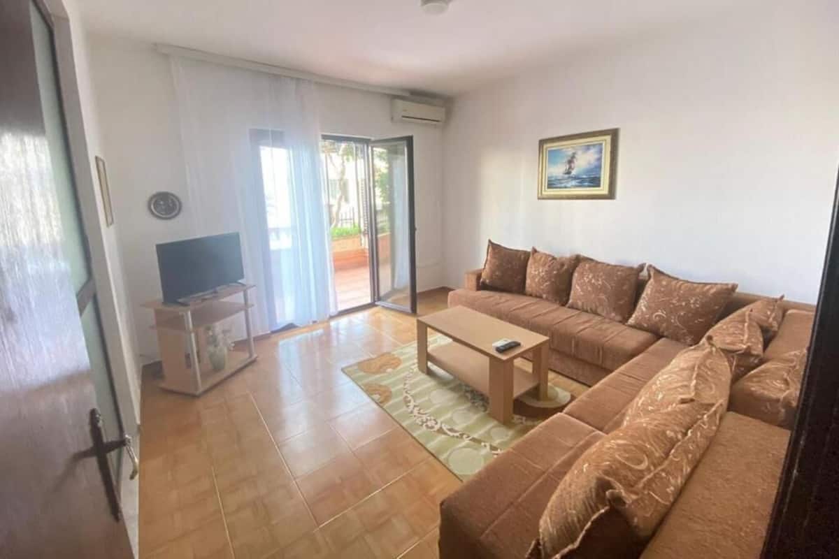 A living room with a sofa, a coffee table, a TV on a stand, and a sliding glass door leading to a balcony.