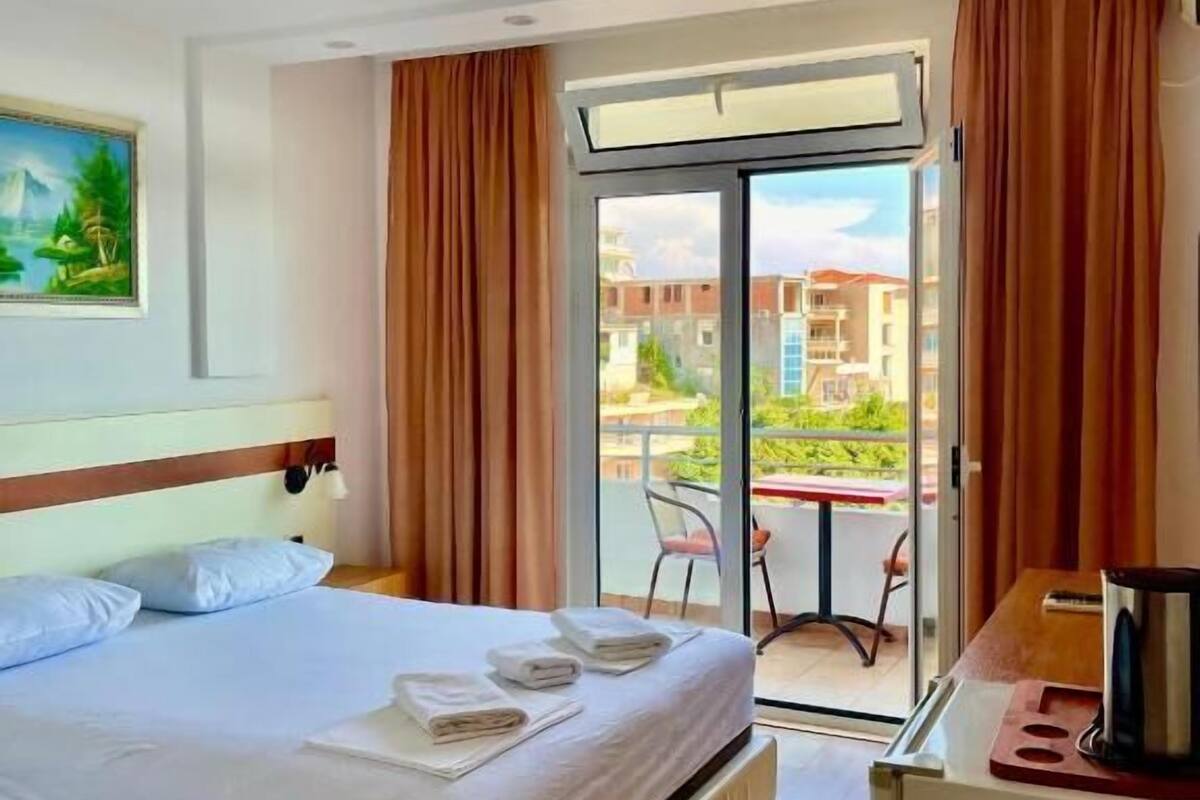 A hotel room with a bed, a desk, a chair, and a view of the outside.
