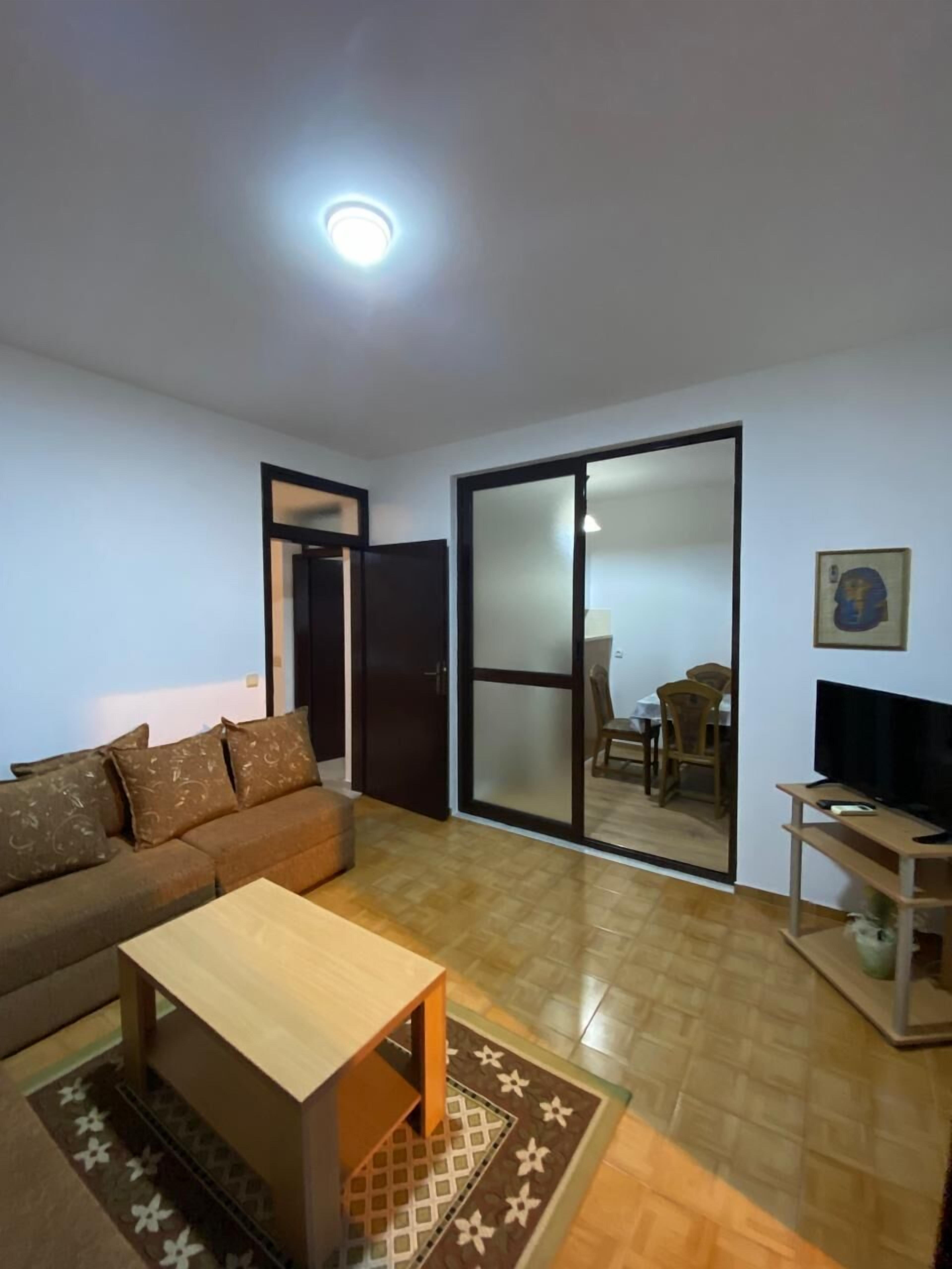 A living room with a sofa, a coffee table, a TV stand, and a sliding glass door leading to a dining area.