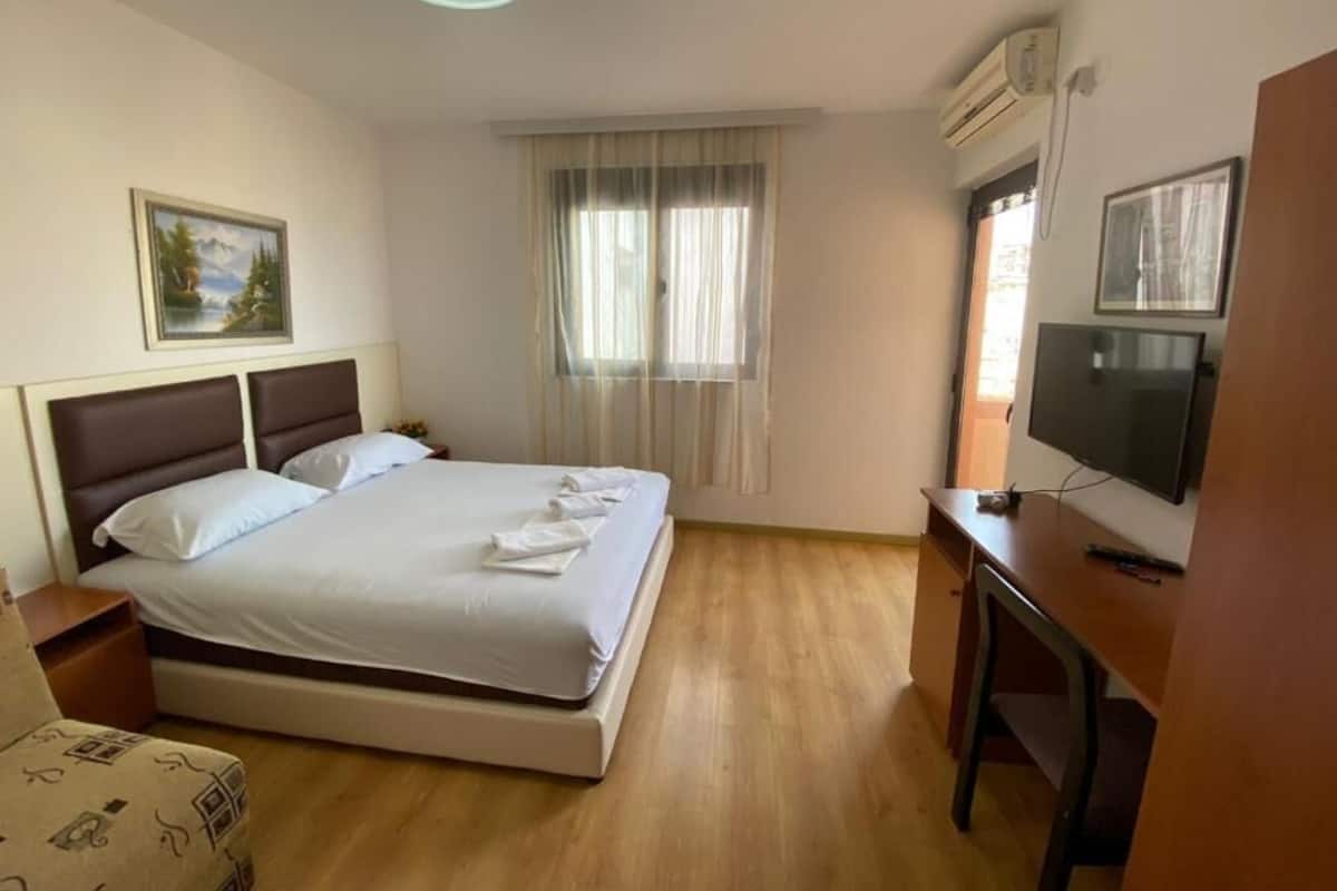 A hotel room with a bed, a desk, a television, and a window with curtains.