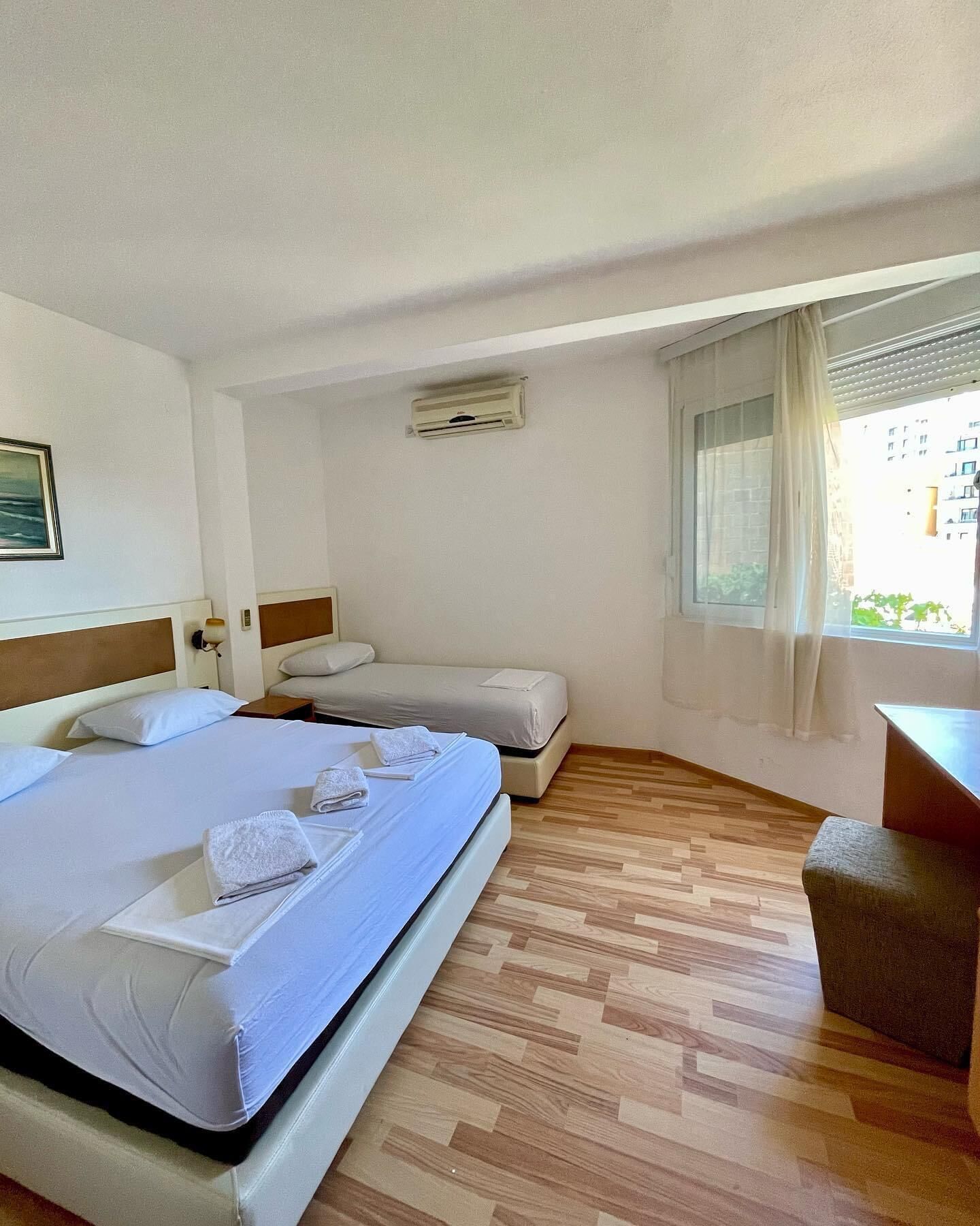 Une chambre d’hôtel avec un grand lit, un plus petit lit, un bureau et une fenêtre avec des rideaux.