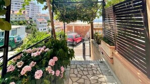 A balcony with a stone floor, a pergola covered with greenery, and pink flowers. - Adriatic (Ulcinj)