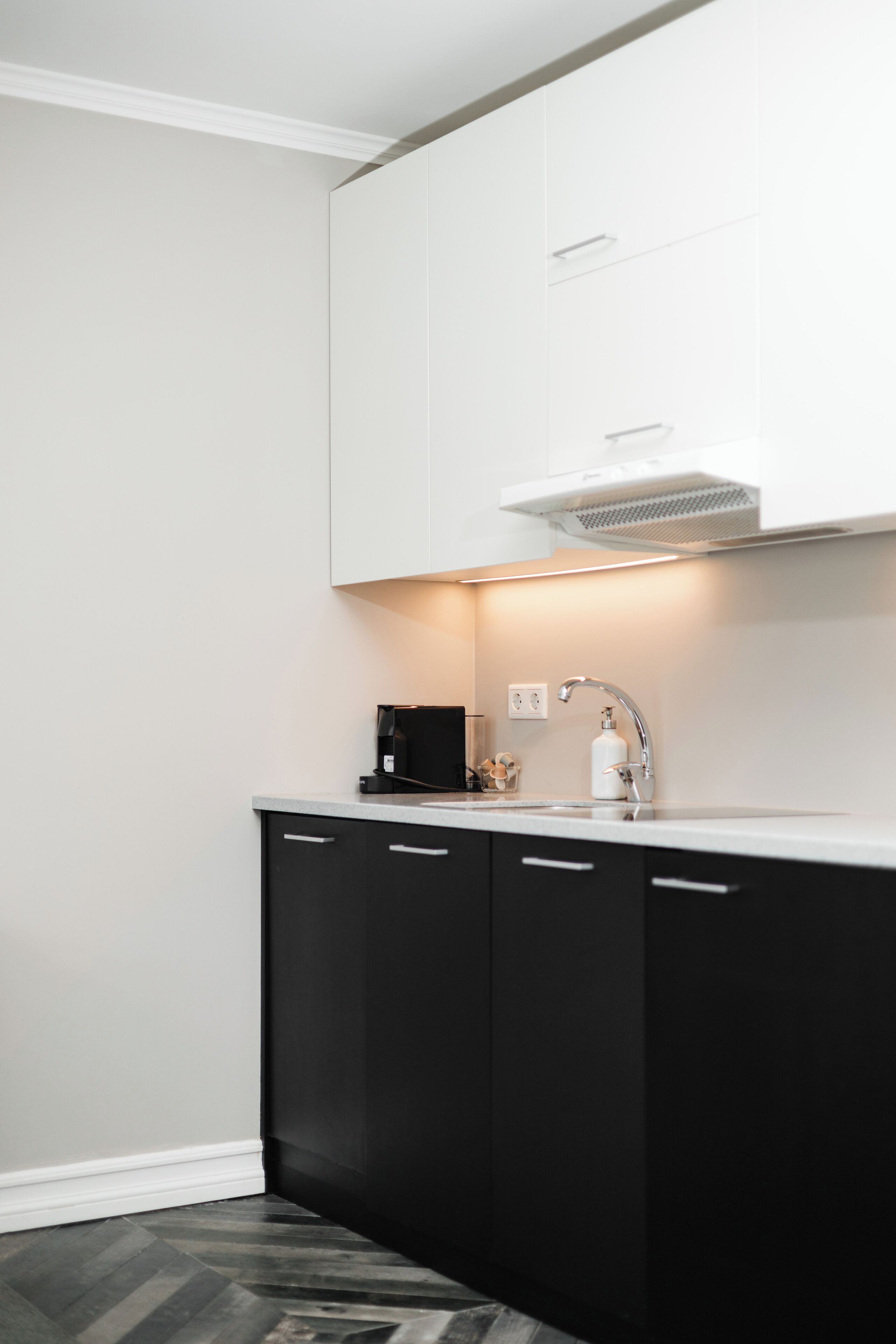 Een moderne keuken met een wit aanrecht, zwarte kastjes en een roestvrijstalen spoelbak, plus een koffieapparaat.