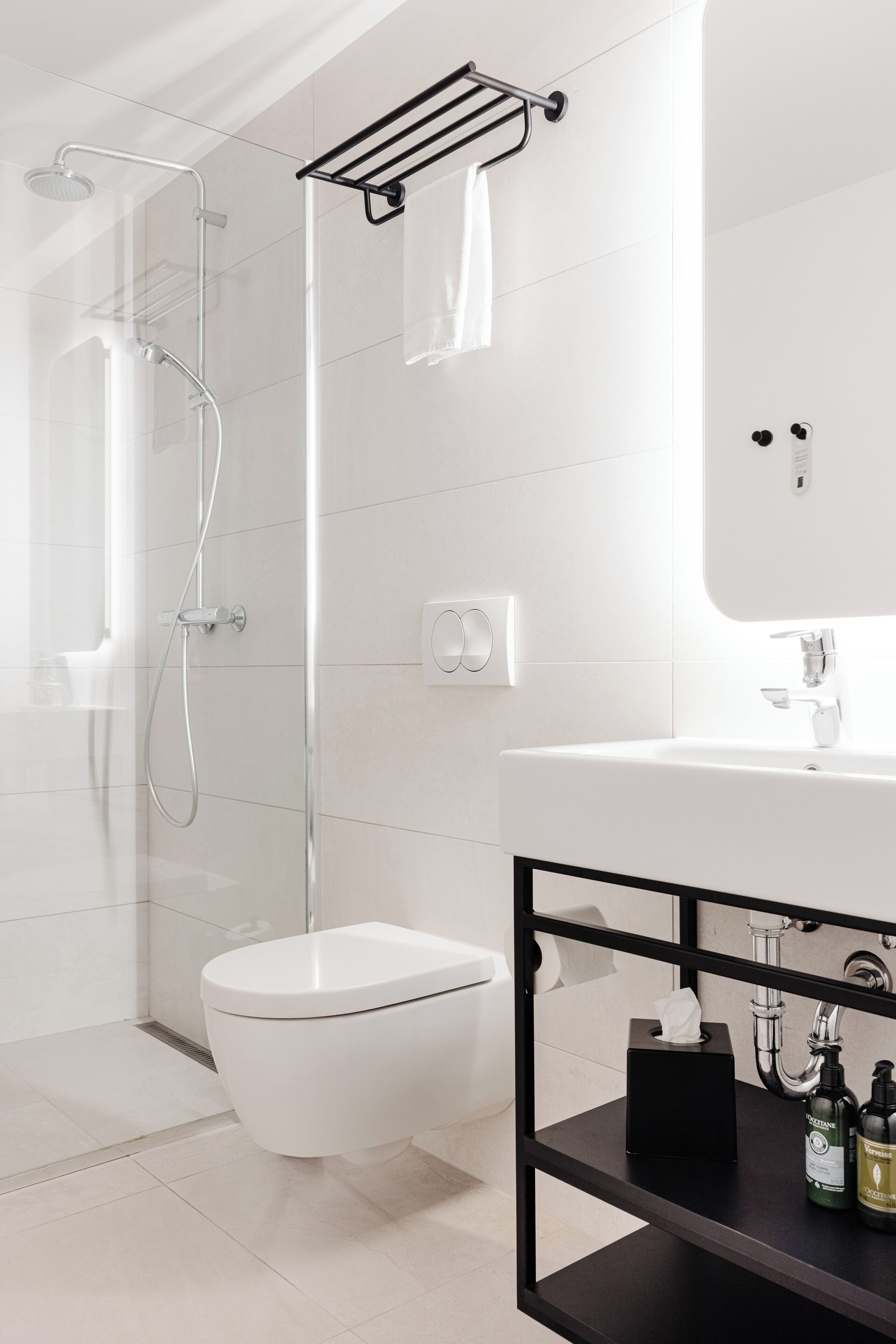 A modern bathroom with a glass-enclosed shower, a white toilet, and a black vanity with toiletries.