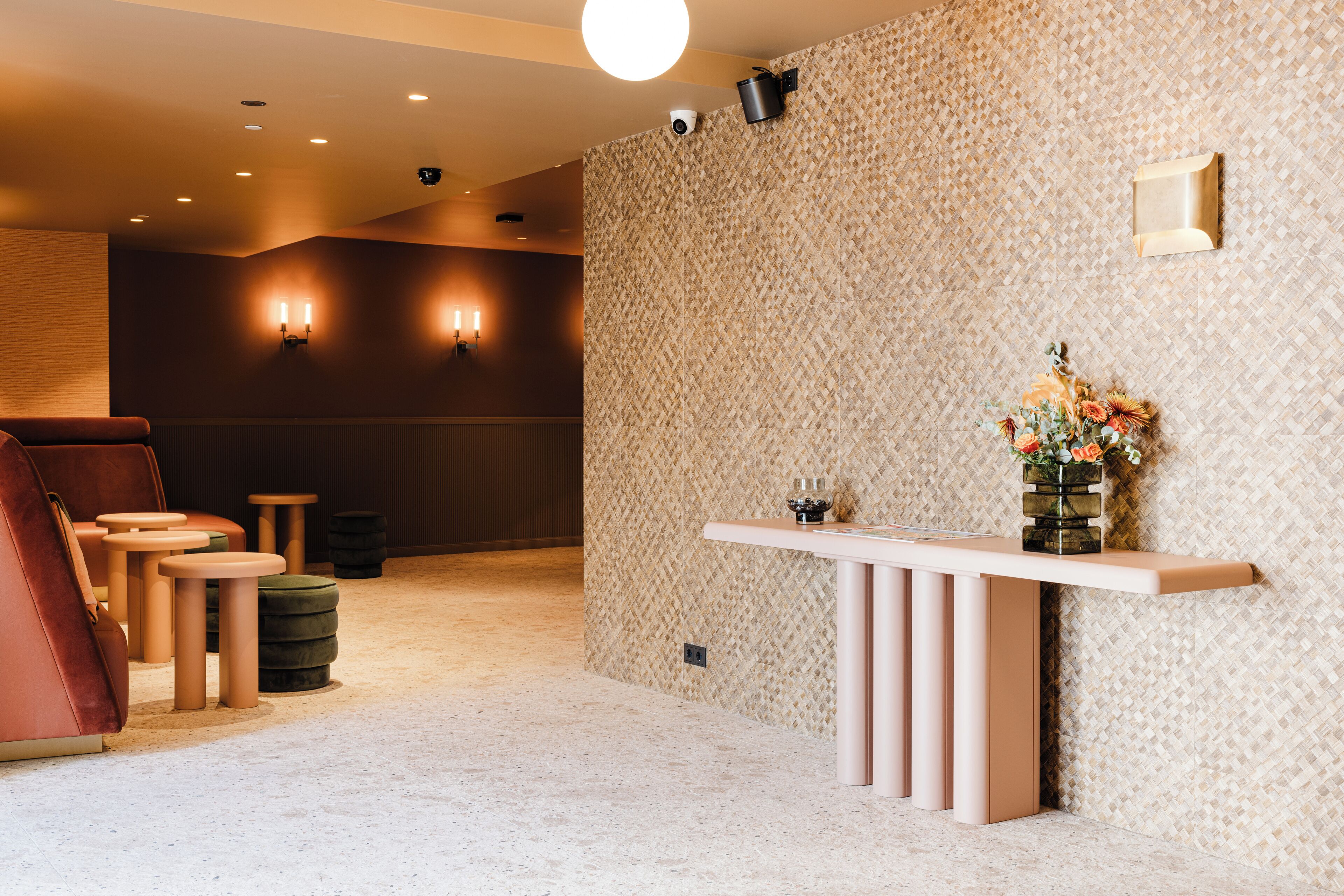 A reception area with a patterned wall, a reception desk, a seating area with chairs and ottomans, and wall-mounted lighting.