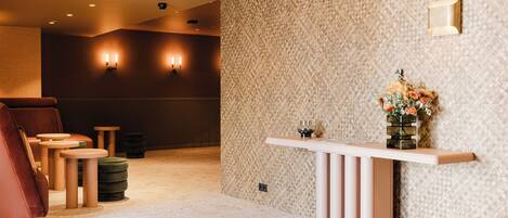 A reception area with a patterned wall, a reception desk, a seating area with chairs and ottomans, and wall-mounted lighting.