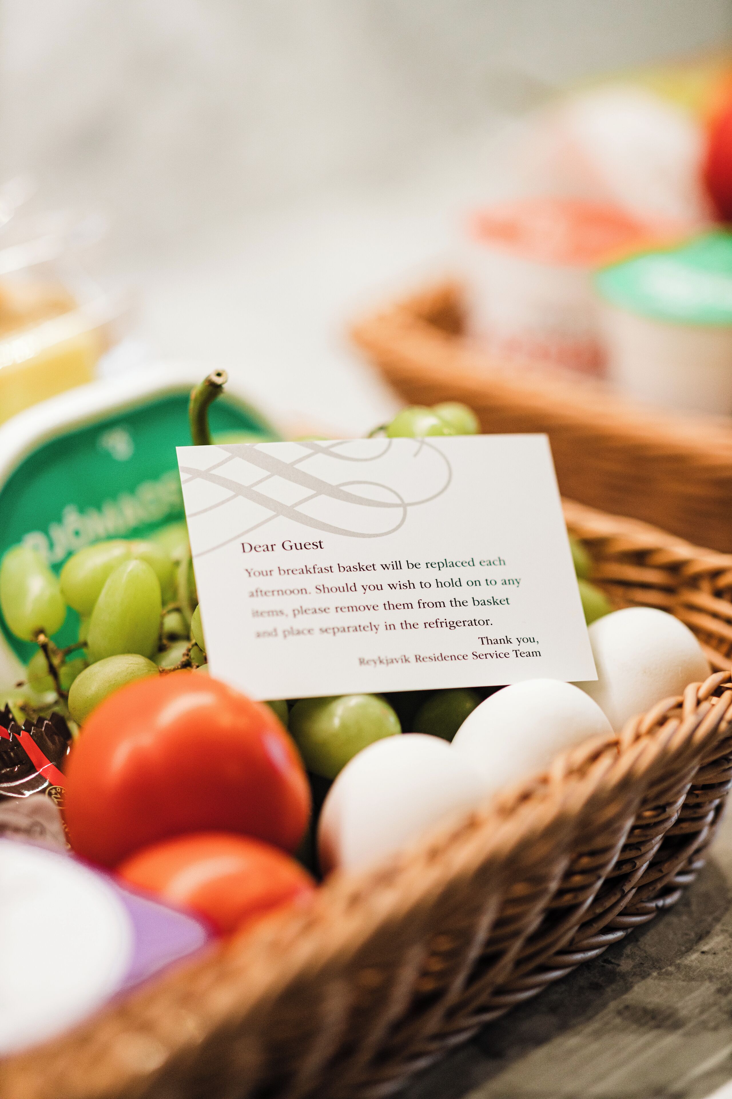 A breakfast basket with a note, containing grapes, tomatoes, and eggs.