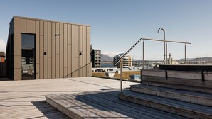 A modern building with a wooden deck, a metal staircase, and a view of the cityscape.