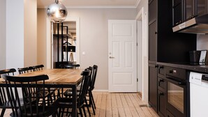 A dining area with a wooden table and black chairs, a modern pendant light, and a kitchen with black cabinets and a white dishwasher.