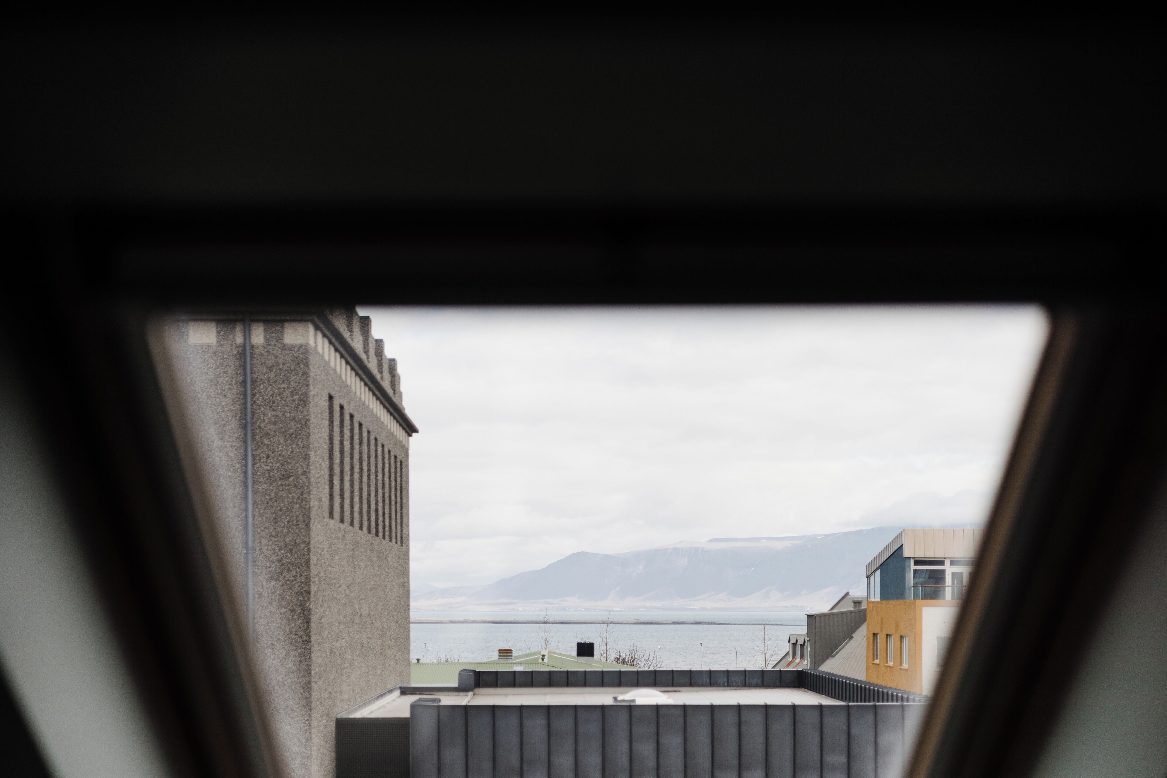 A view from a window overlooking a cityscape with buildings and a body of water in the distance.