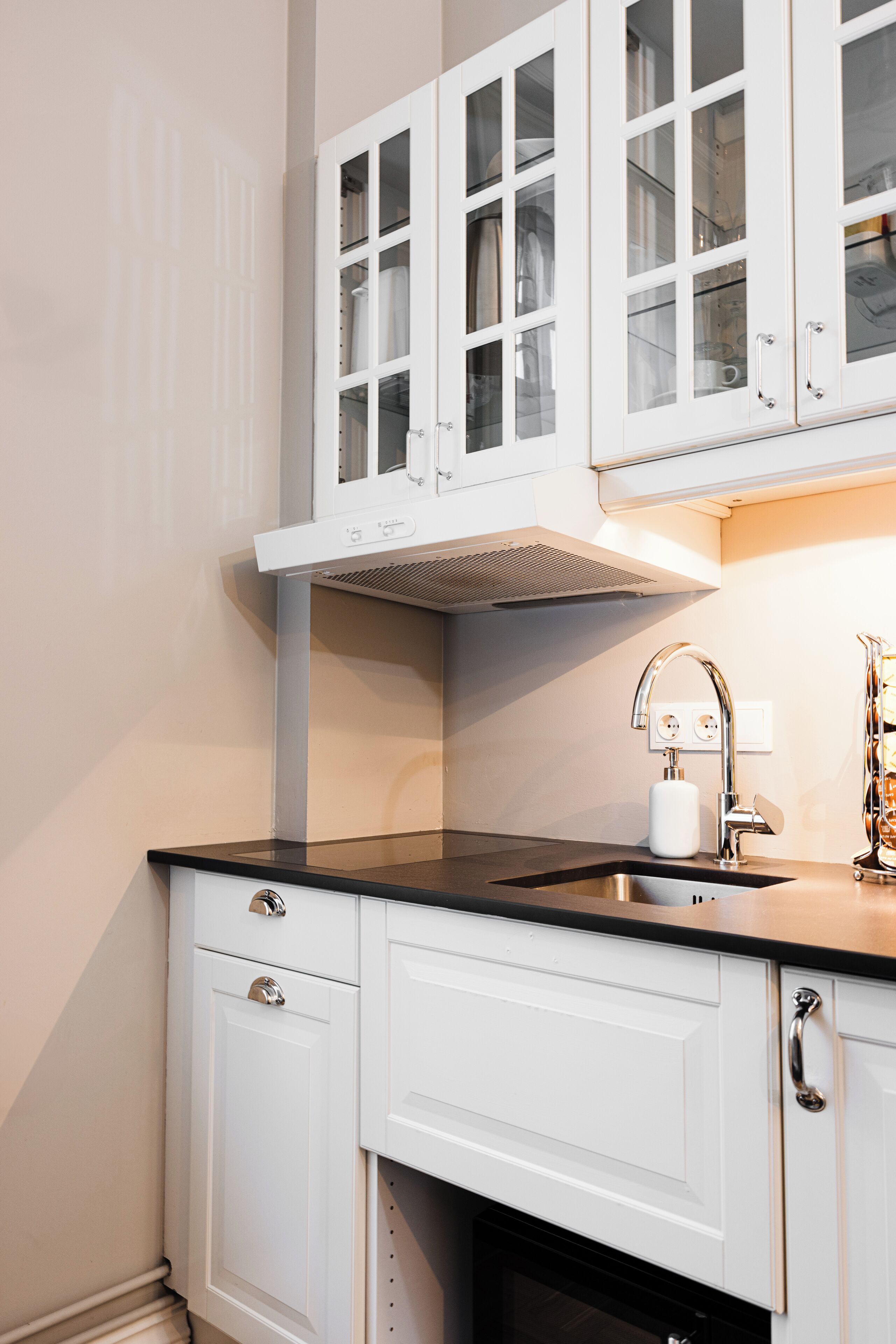 A kitchen with white cabinets, a black countertop, a stainless steel sink, and a range hood.