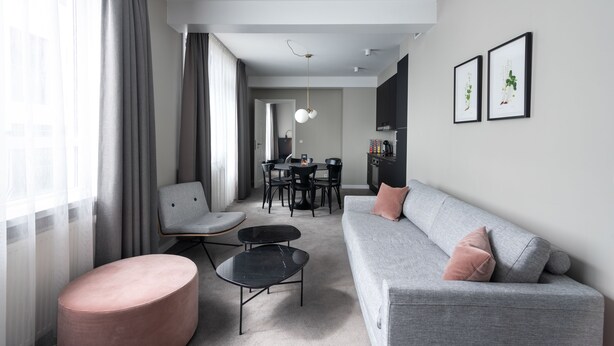 A modern living room with a grey sofa, a pink ottoman, a black coffee table, and a dining area with a round table and chairs.