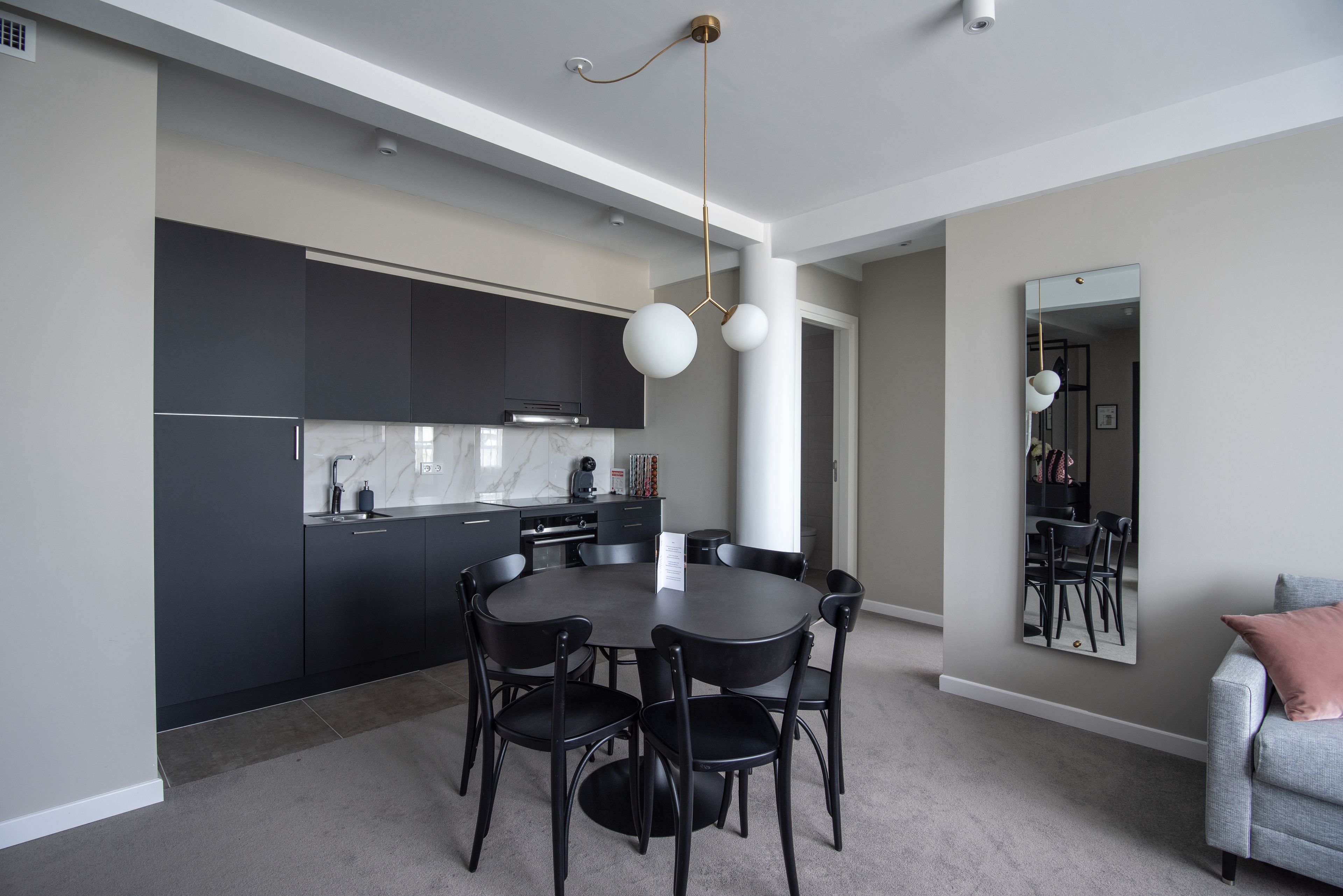 A modern kitchen with dark cabinetry, a marble countertop, and a round dining table with chairs.