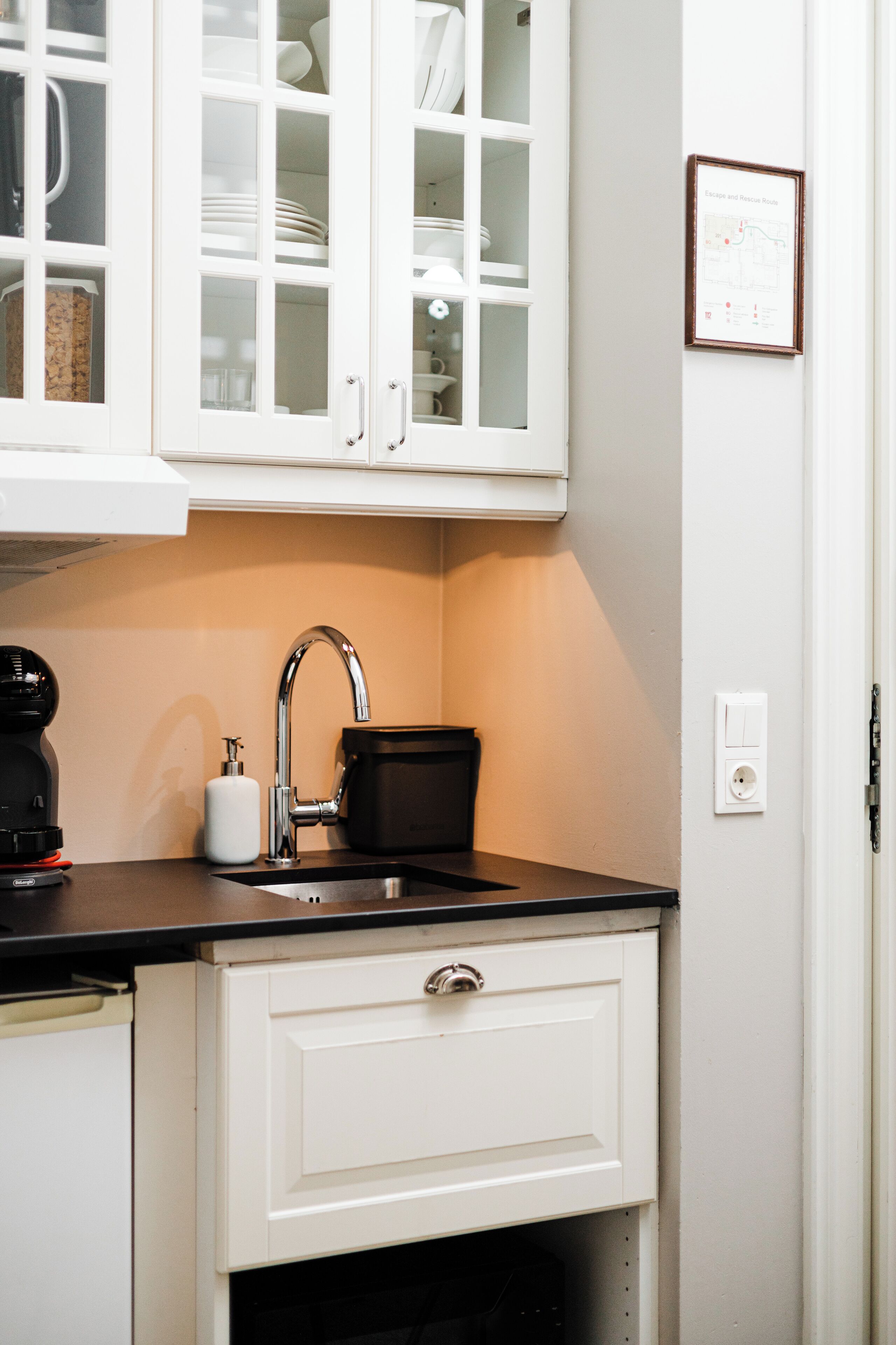 A kitchen with white cabinets, a black countertop, a sink, and a coffee maker.
