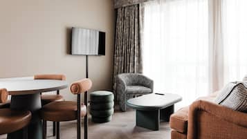 A modern living room with a round table, brown leather chairs, a grey armchair, and a television mounted on the wall.