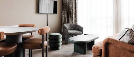 A modern living room with a round table, brown leather chairs, a grey armchair, and a television mounted on the wall.