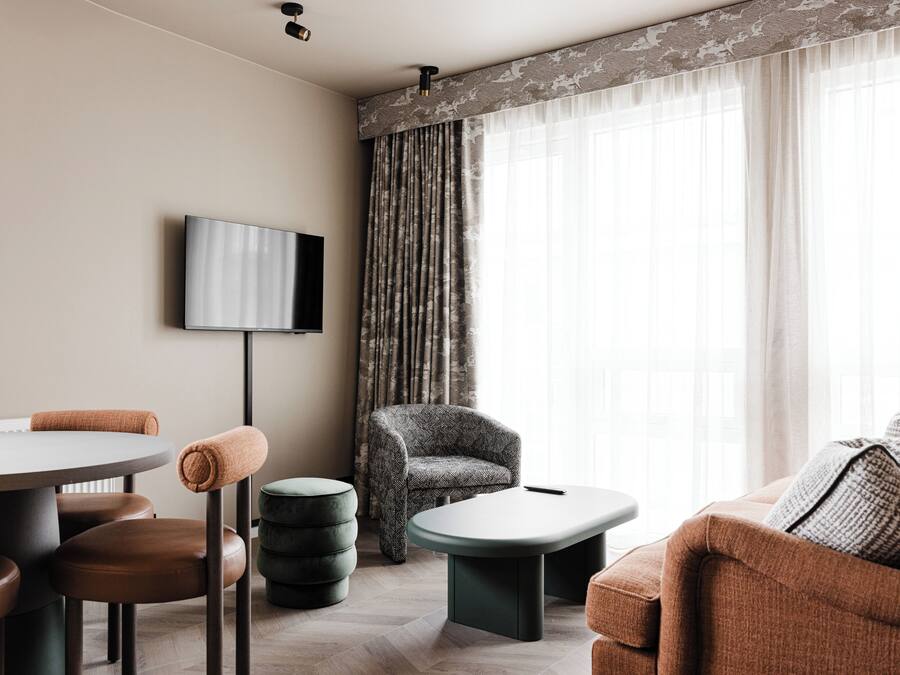 Una sala de estar moderna con una mesa redonda, sillas de cuero marrón, un sillón gris y un televisor montado en la pared.
