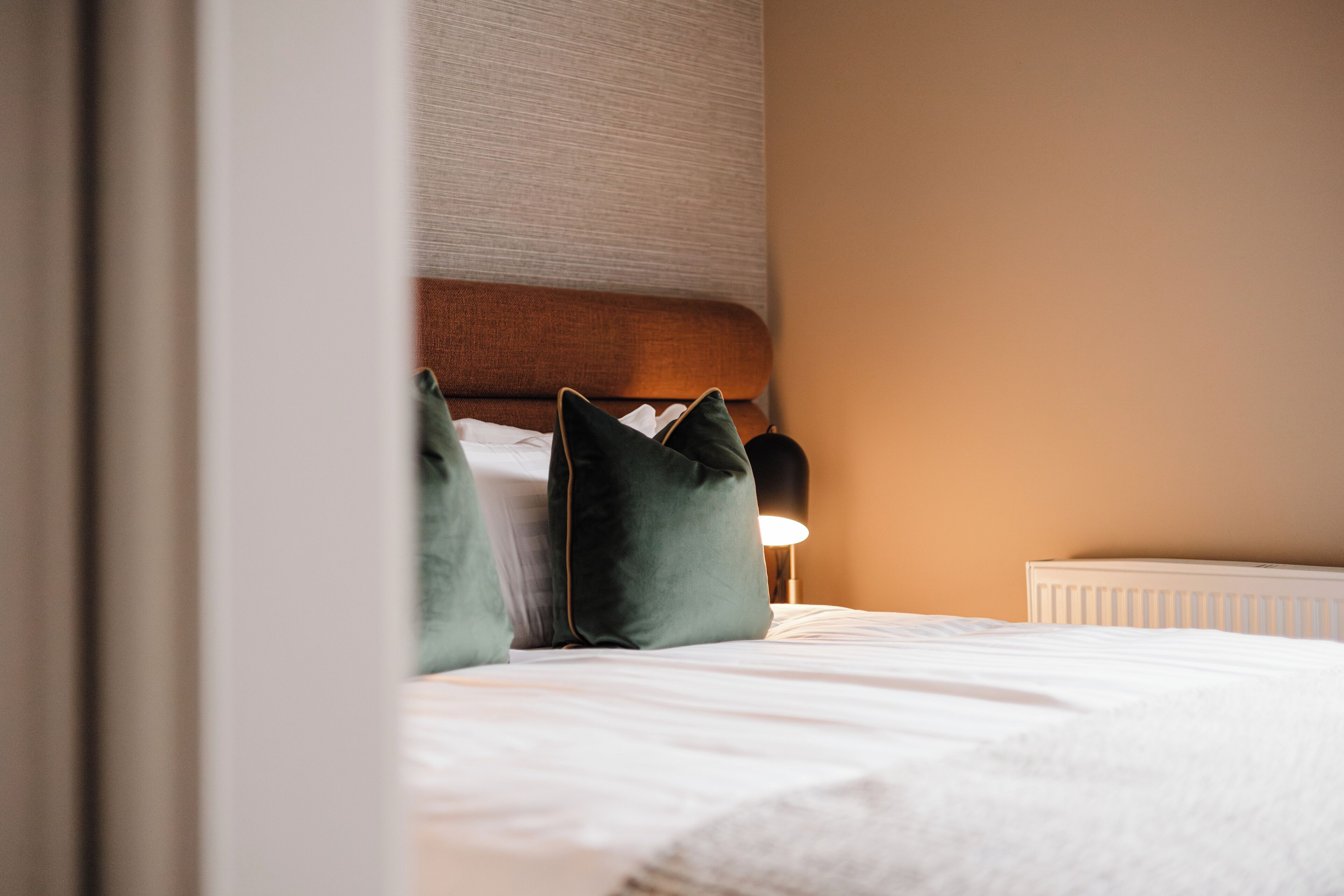 A neatly made bed with pillows, a bedside lamp, and a radiator.