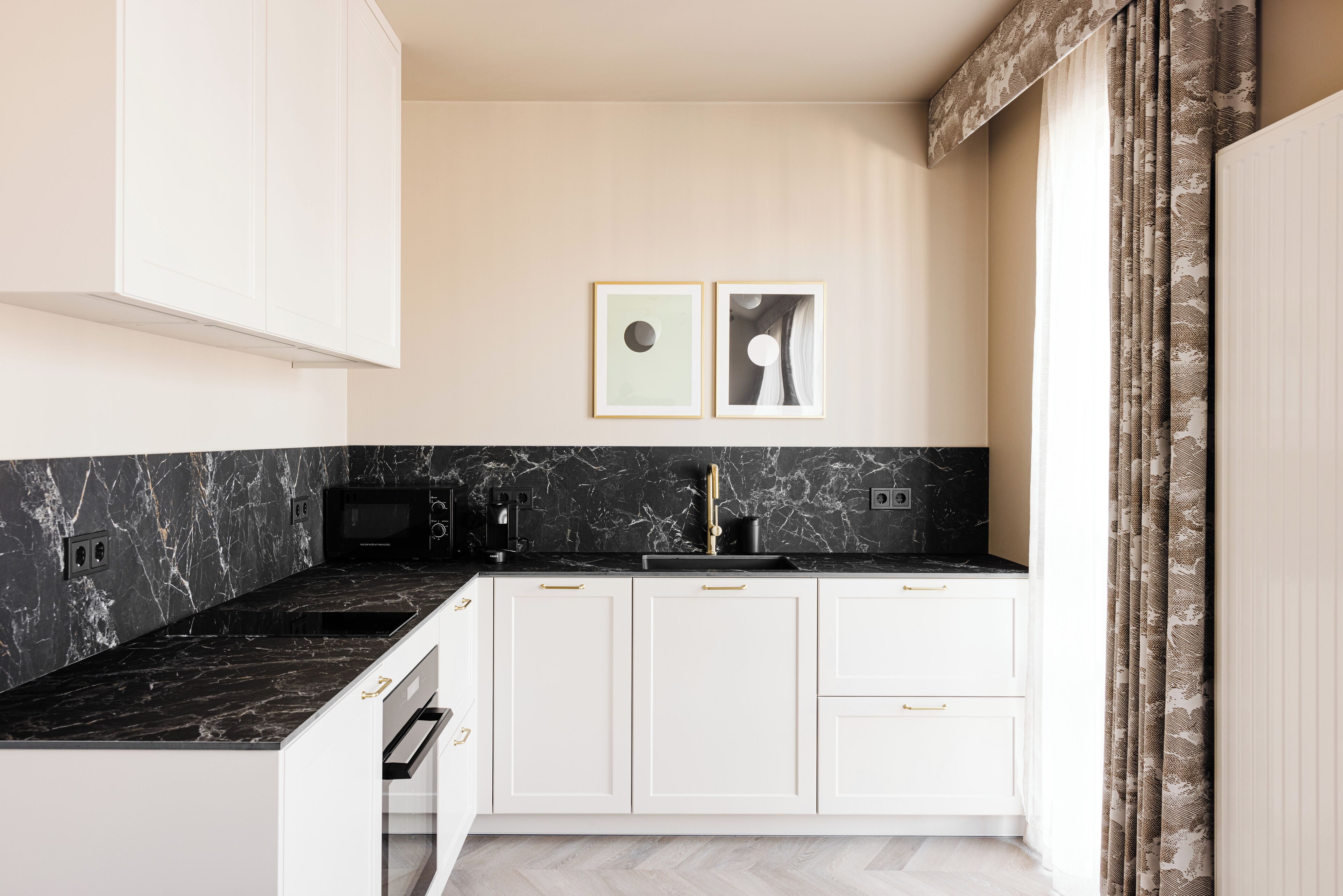 A modern kitchen with white cabinets, a black marble countertop, and a black microwave.