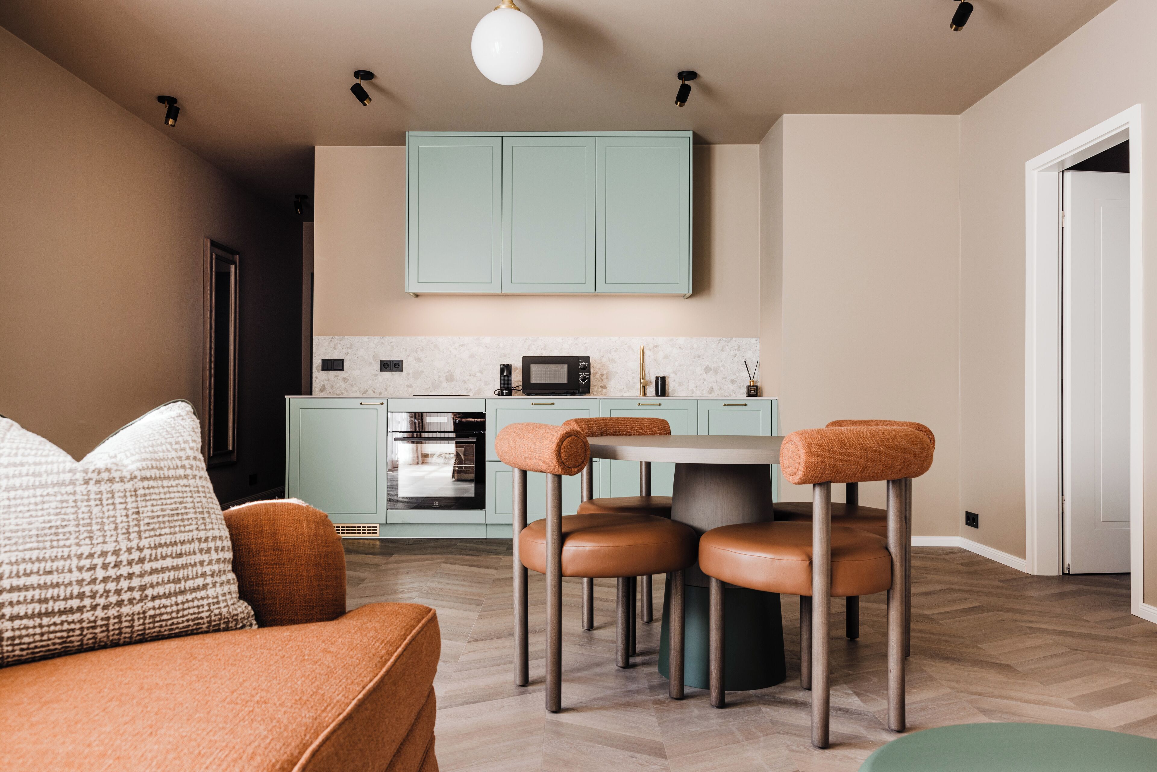 A modern living room with a sofa, a dining table with chairs, and a kitchen area with cabinets and appliances.