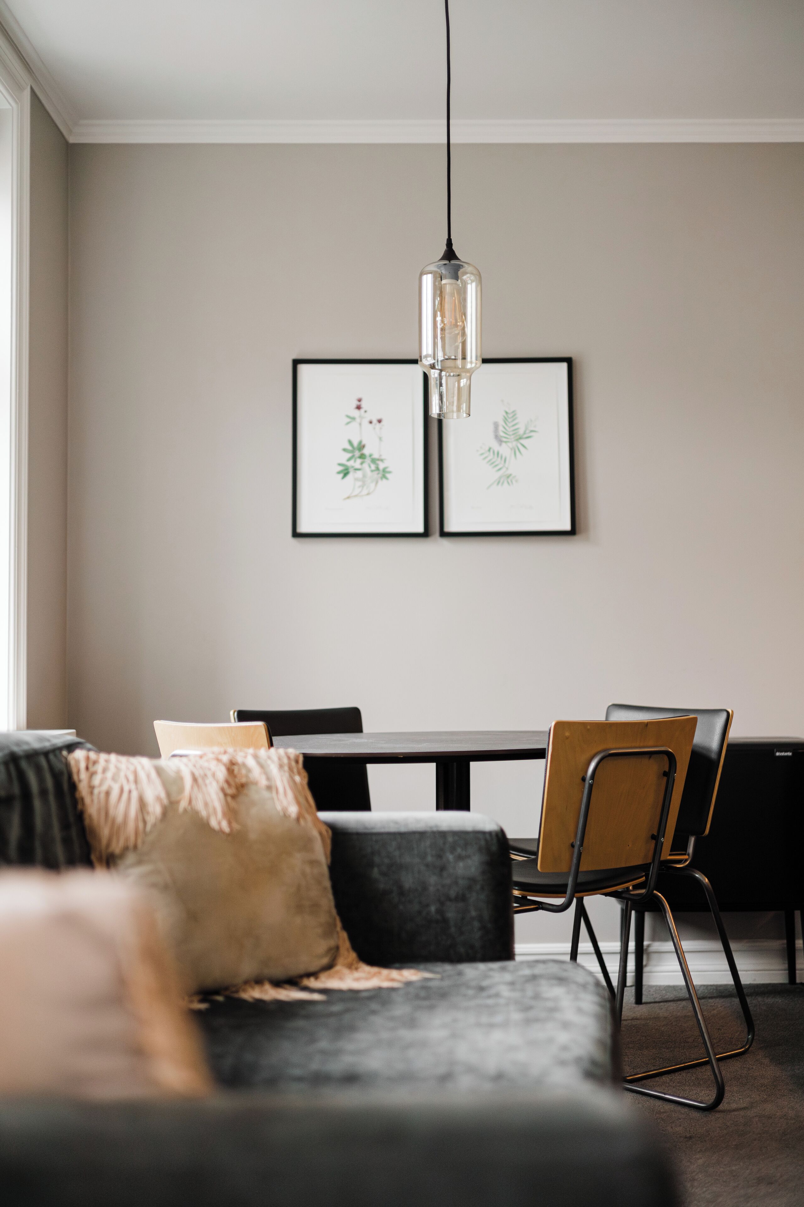A modern living room with a sofa, a dining table, and chairs. There are framed botanical prints on the wall.
