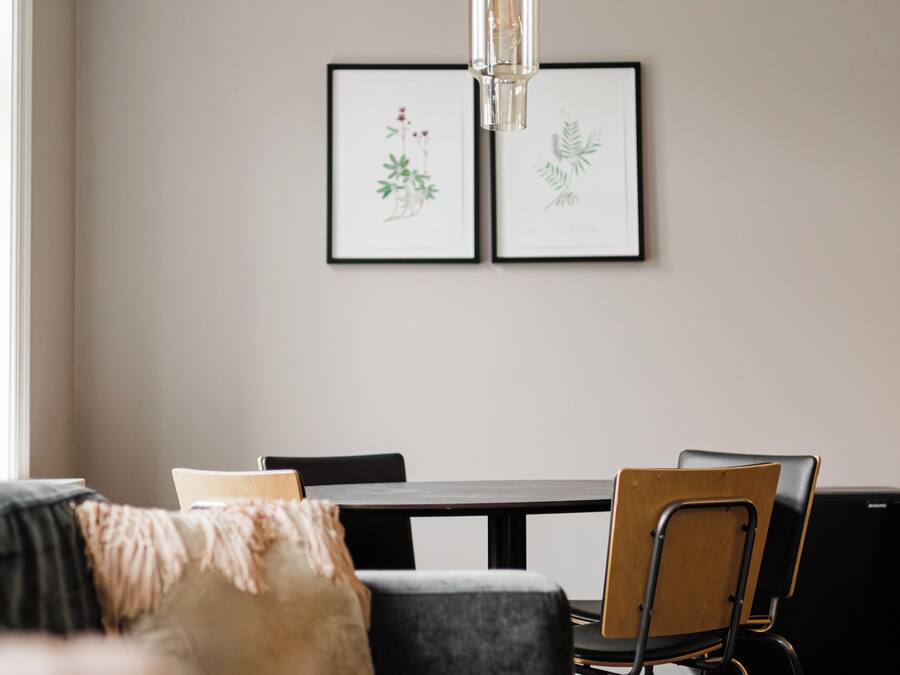 A modern living room with a sofa, a dining table, and chairs. There are framed botanical prints on the wall.