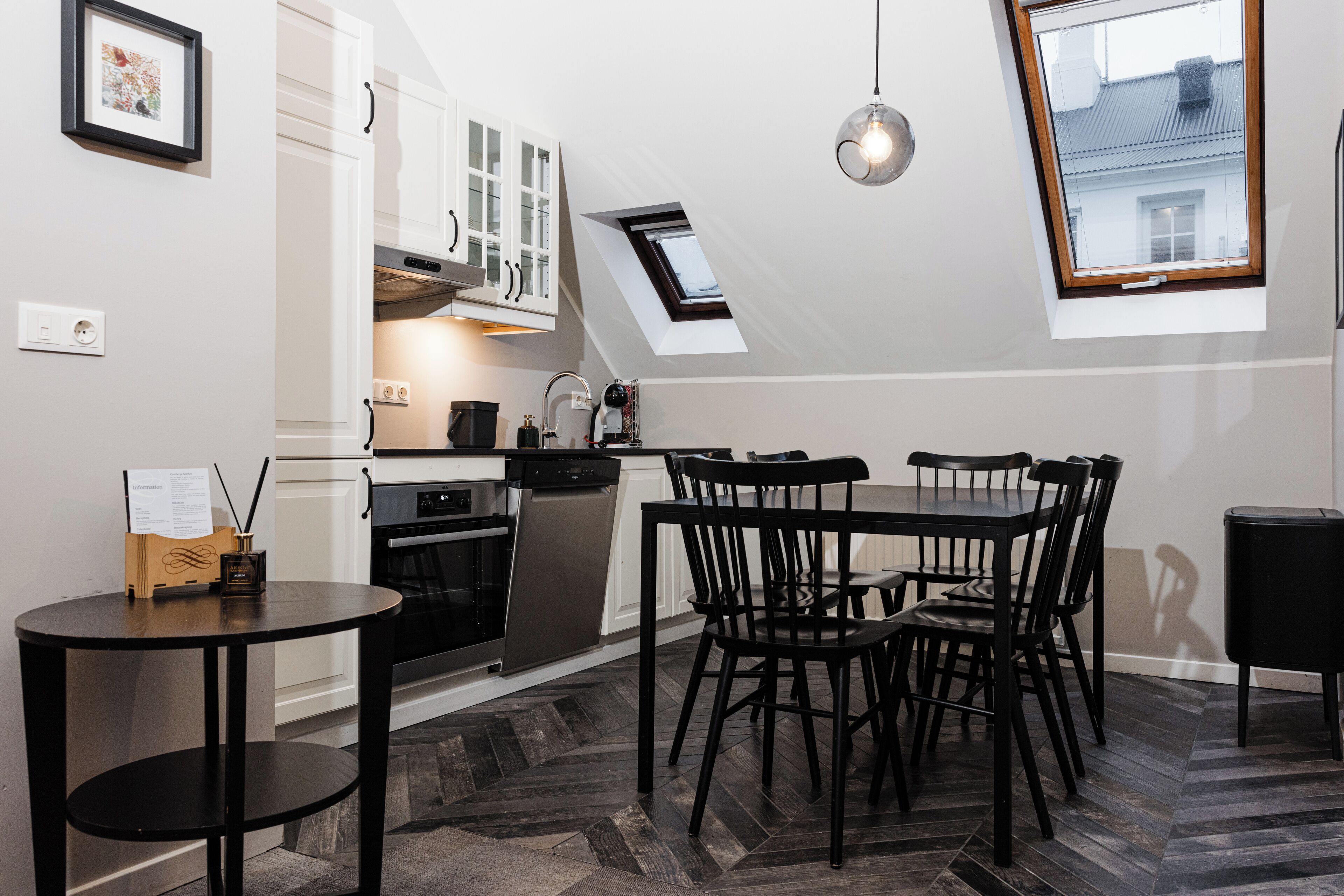 A modern kitchen with white cabinets, a black dining table, and a herringbone-patterned floor.