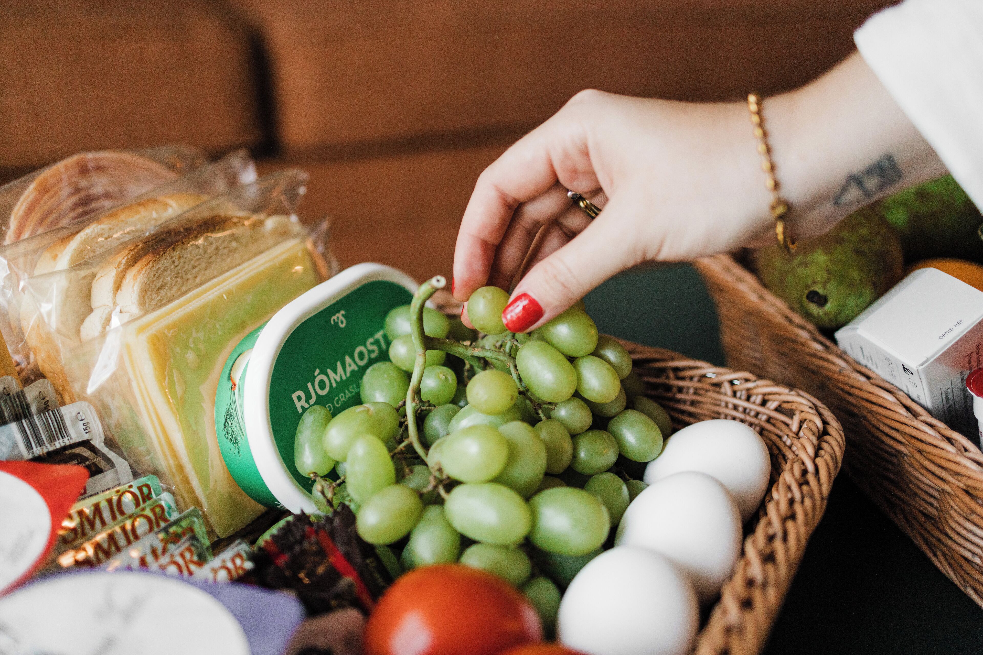 Una cesta llena de uvas verdes, huevos y tomates.