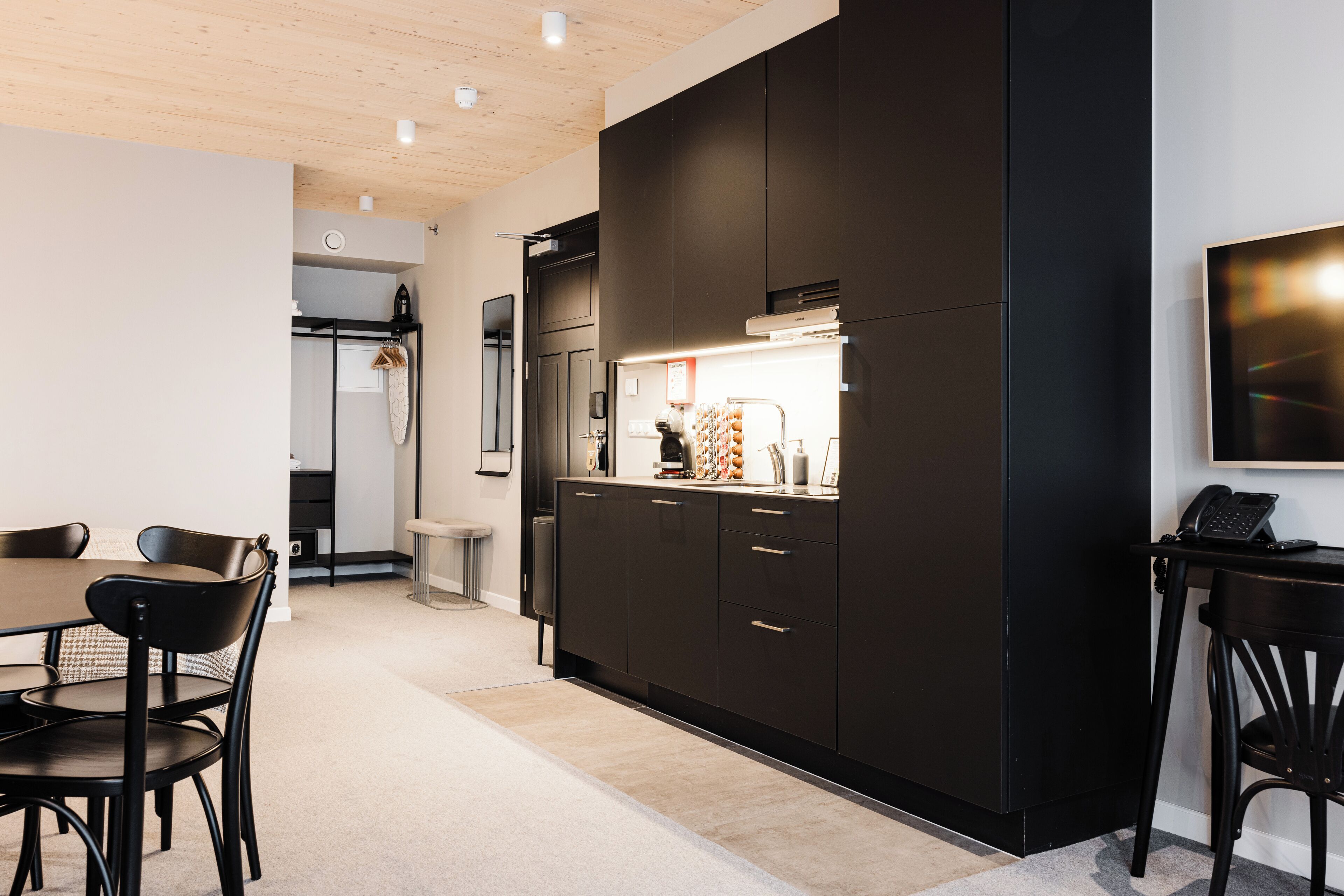 A modern kitchen with dark cabinetry, a dining area with a table and chairs, and a visible bathroom with a shower.