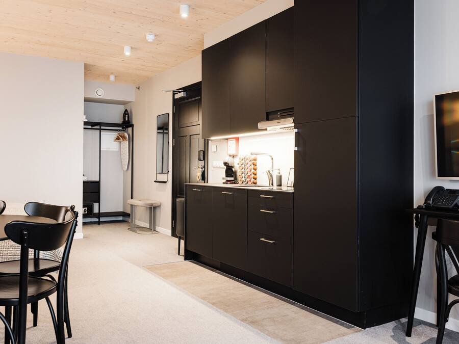 A modern kitchen with dark cabinetry, a dining area with a table and chairs, and a visible bathroom with a shower.