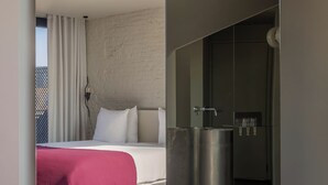A modern hotel room with a large bed, a red throw blanket, and a small bathroom with a sink and mirror.