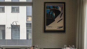 A restaurant with a brick floor, wooden chairs, a round table, and a framed abstract painting on the wall.