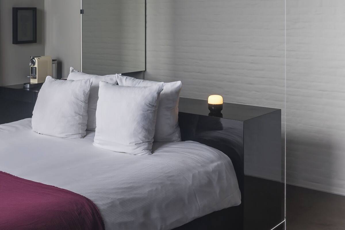 A modern bedroom with a large bed, a bedside table with a lamp, and a framed picture on the wall.
