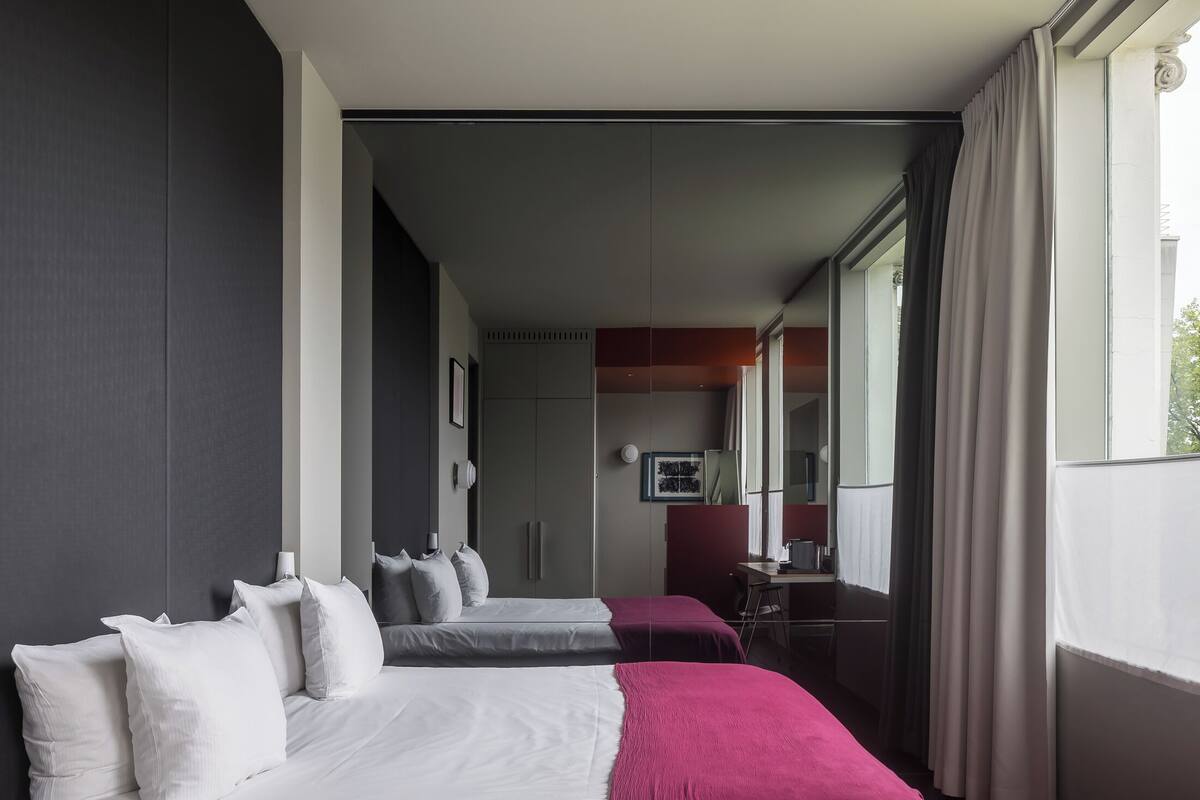 A hotel room with two beds, a desk, and a large window.