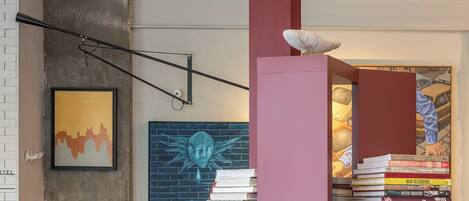 A modern interior with a high ceiling, a central red pillar, a bookshelf with books, and a seating area with a table and chairs.
