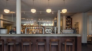 A bar area with a long counter, multiple stools, hanging pendant lights, and a variety of bottles and glasses.