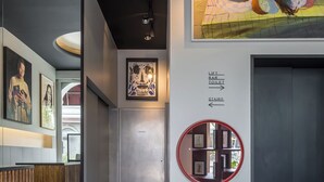 A hallway with a reception desk, artwork on the walls, directional signs, and an elevator.