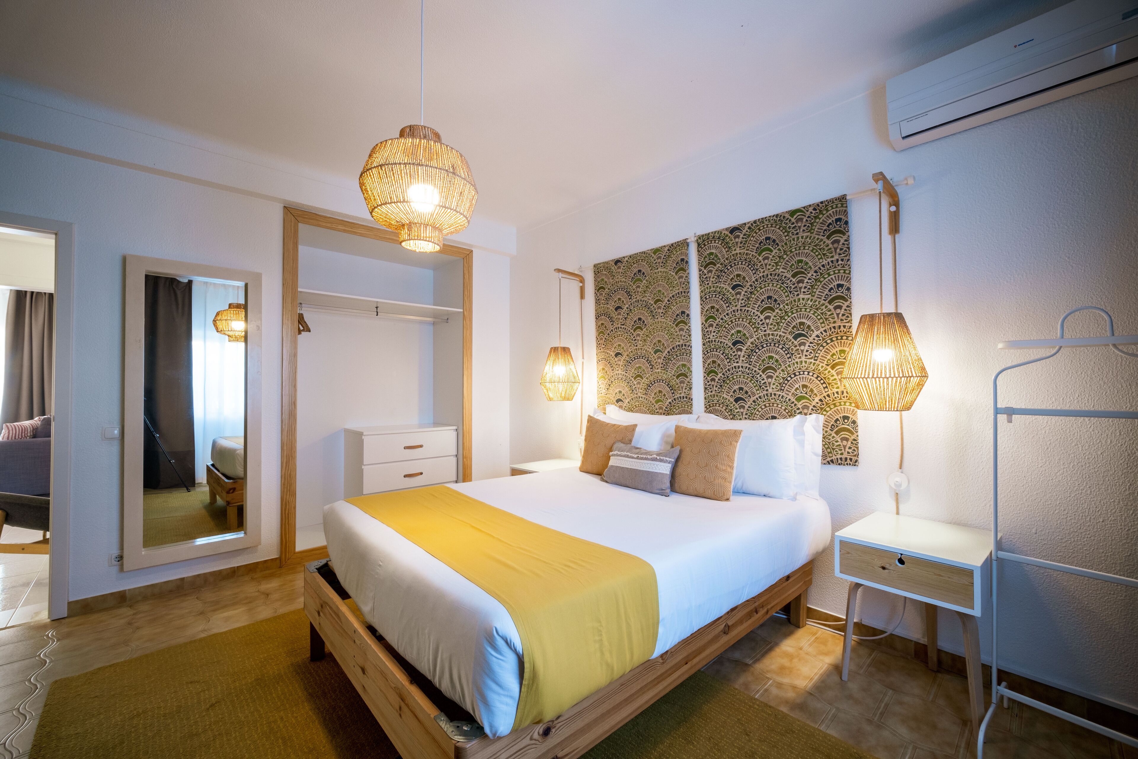 A bedroom with a bed, bedside table, wall-mounted lamp, and a mirror.