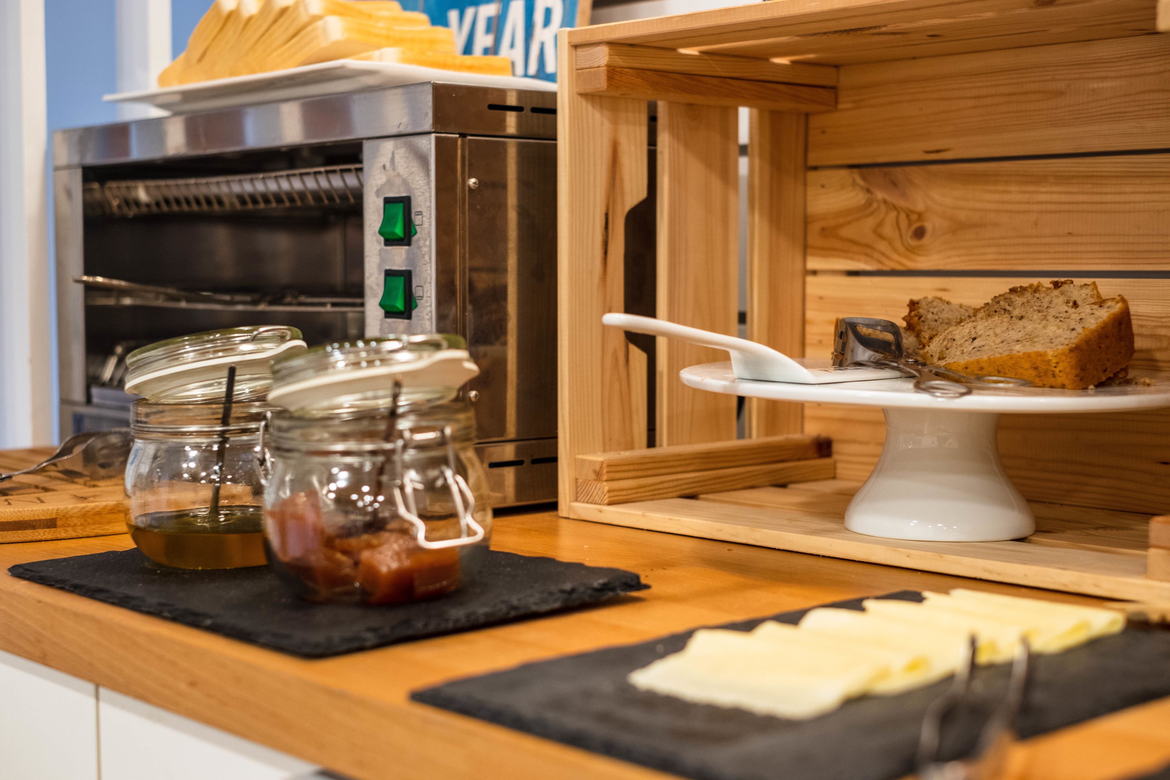 A kitchen counter with a bread loaf on a white cake stand, a stainless steel oven, and two glass jars with lids.